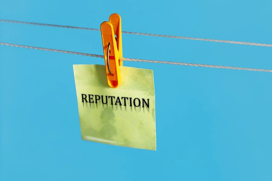 Sticky note with the word “reputation” printed on it hanging from clothesline in front of a blue background.]