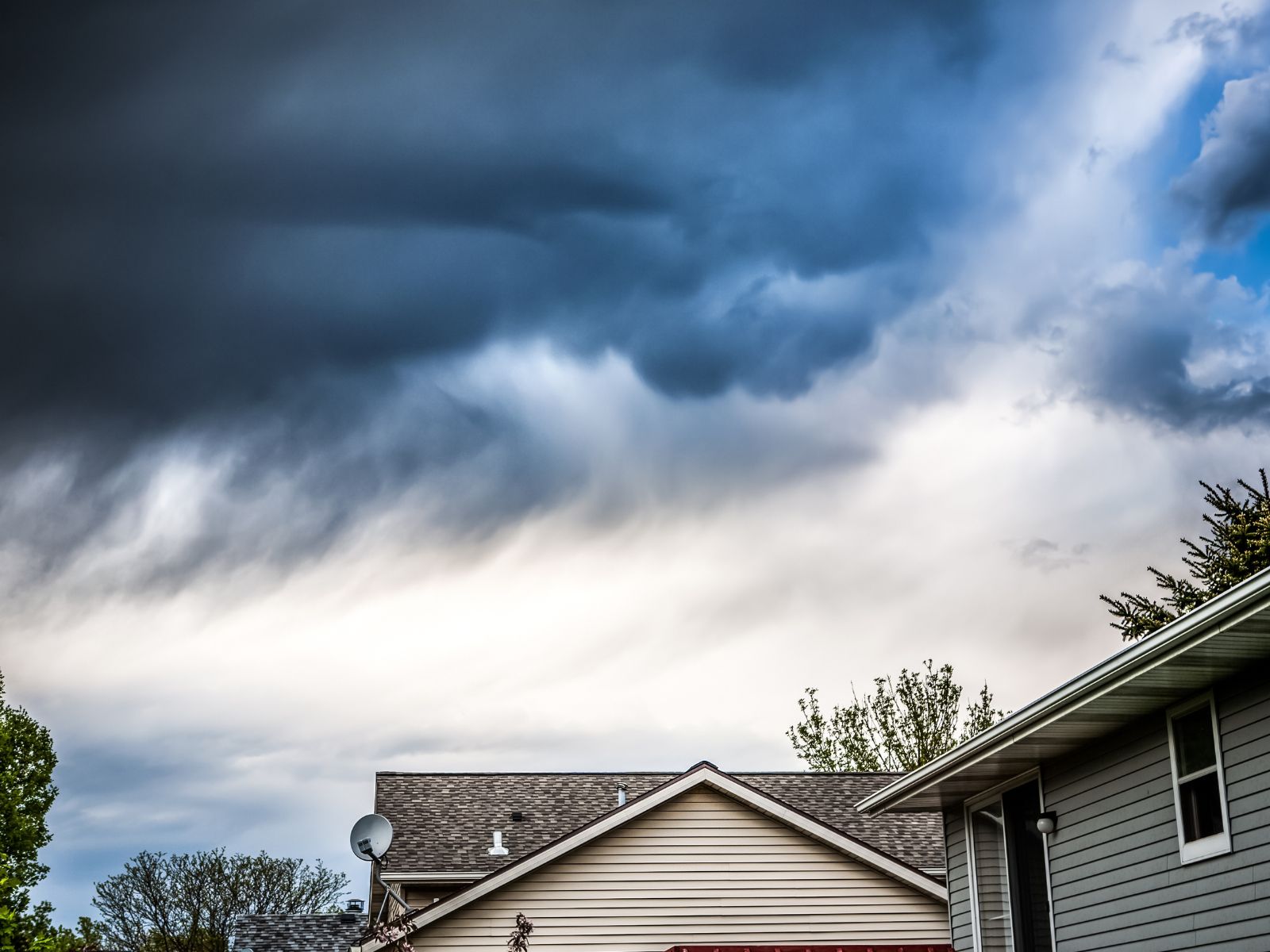 Dark storm clouds over suburban homes—Rooftecco provides storm damage roof inspections and emergency repair services.